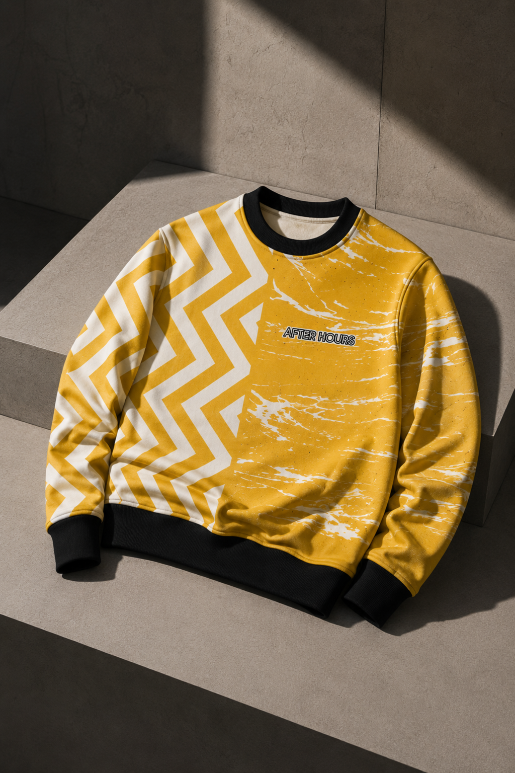 A yellow crew neck sweatshirt with a split design: one side features a bold white chevron pattern, and the other side has a white distressed paint-splatter pattern. It has black ribbed cuffs, collar, and hem, with 'AFTER HOURS' printed in black on the chest.