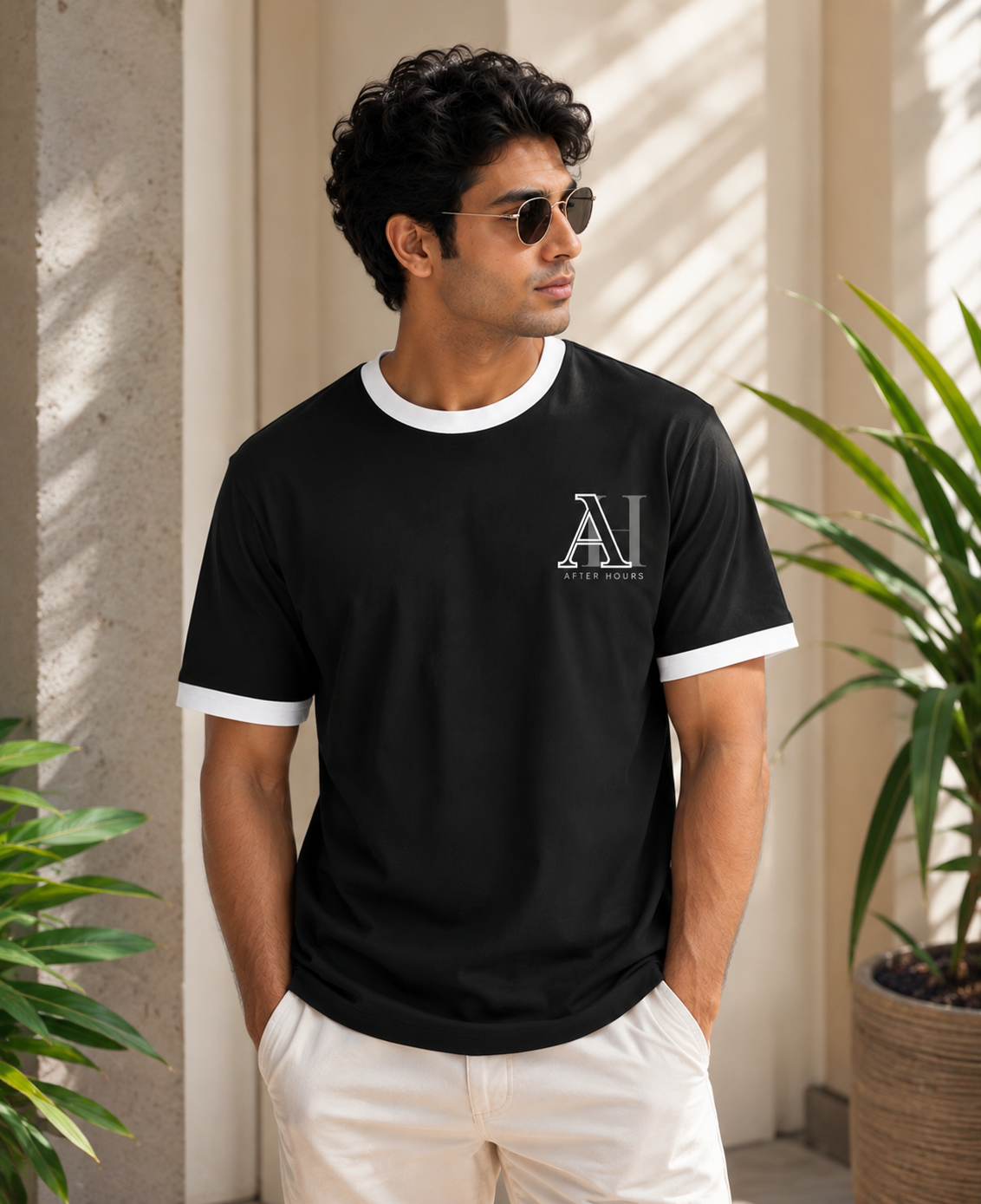 Man wearing a black t-shirt with a logo, standing outdoors with plants around.