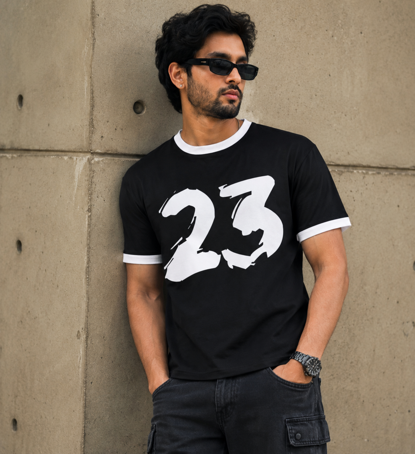 Man wearing a black t-shirt with white 23 number leaning against a concrete wall.