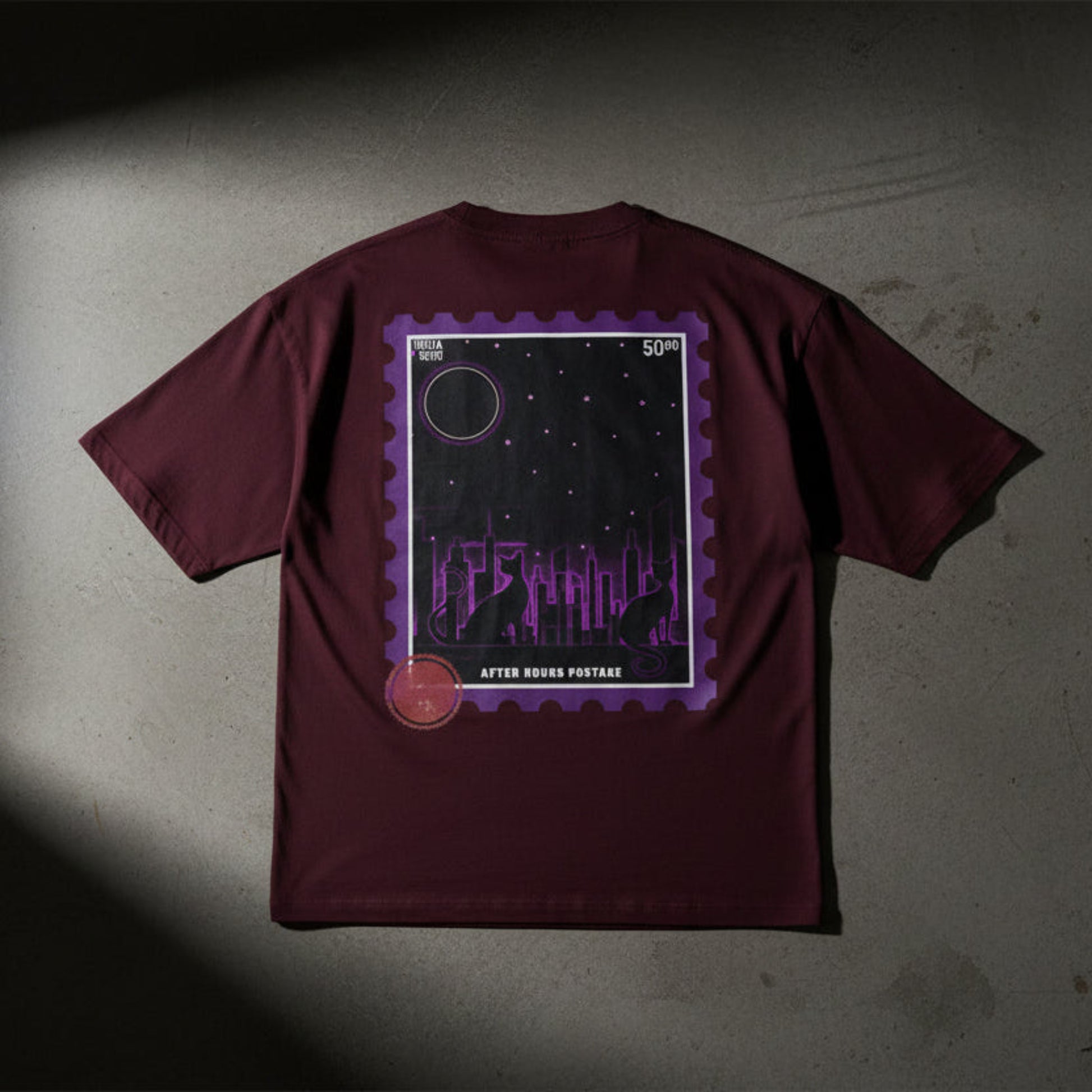 Maroon t-shirt with a purple graphic design on the back against a grey textured wall background