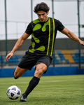 A soccer player in a black and neon green athletic kit dribbling a soccer ball on a green turf field.