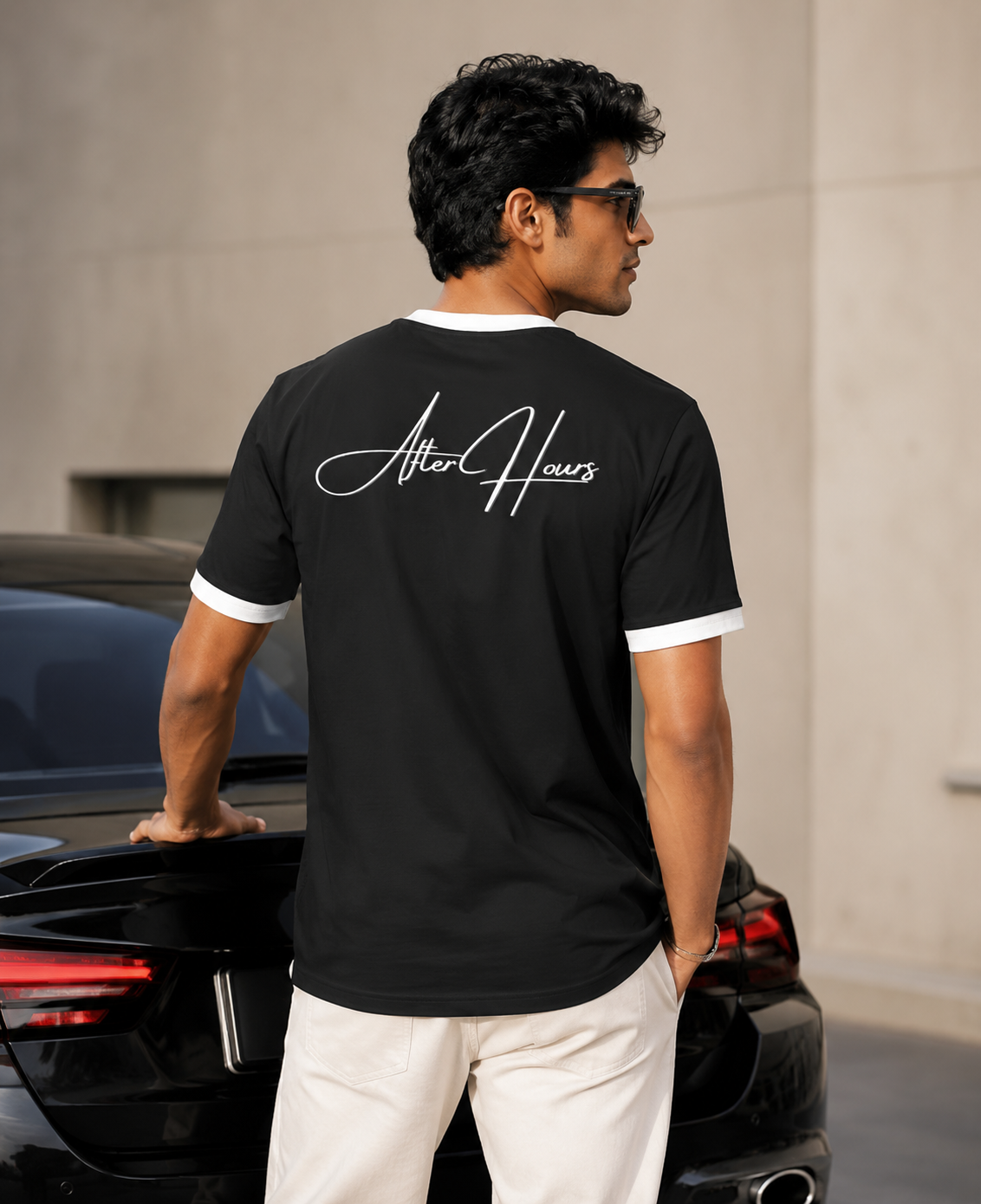 Man wearing a black t-shirt with 'After Hours' logo, standing next to a car.