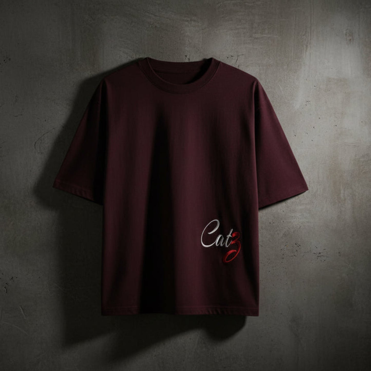 Maroon t-shirt with a logo on a grey textured wall background