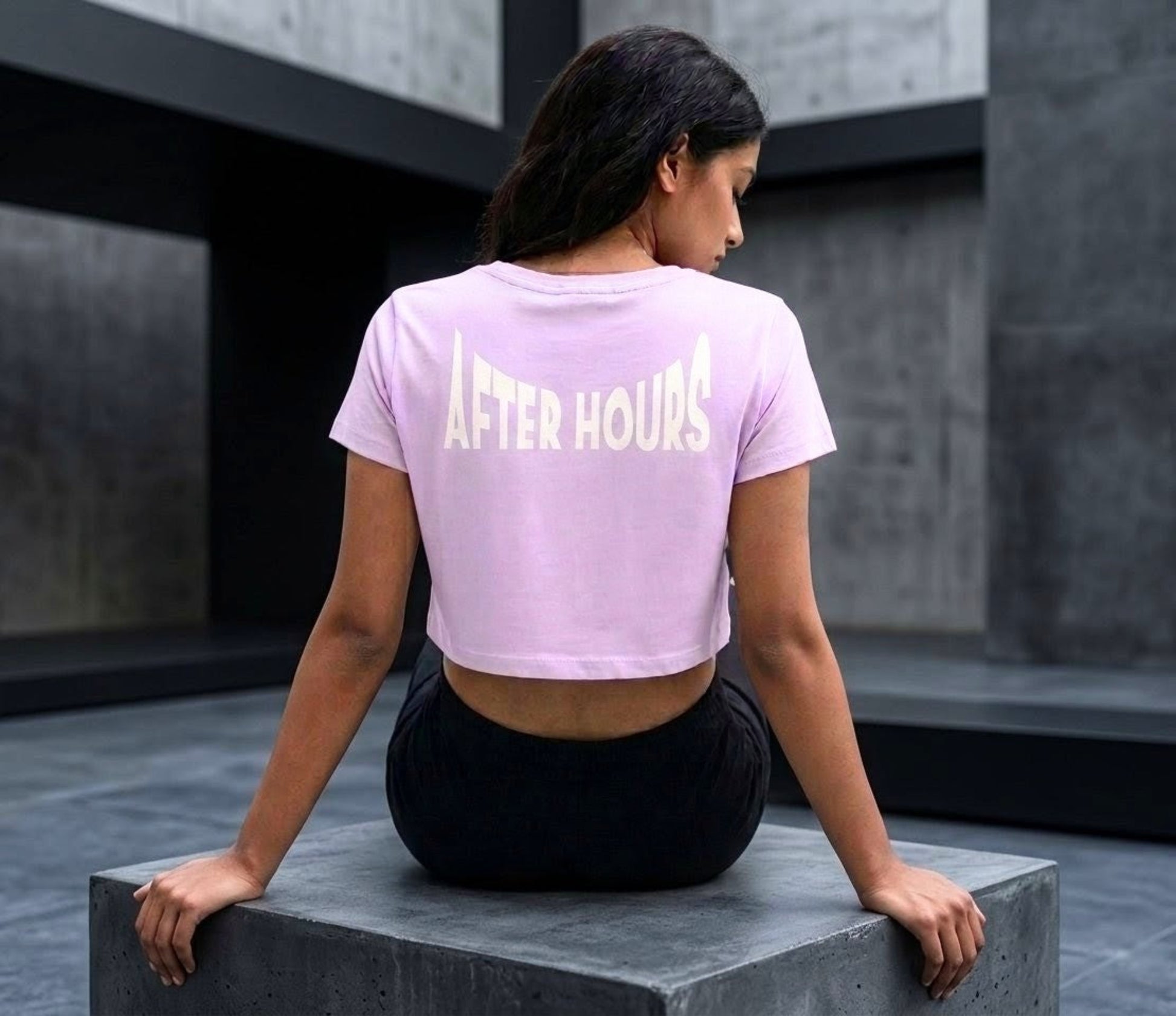 Person wearing a lavender 'After Hours' t-shirt sitting on a concrete block.