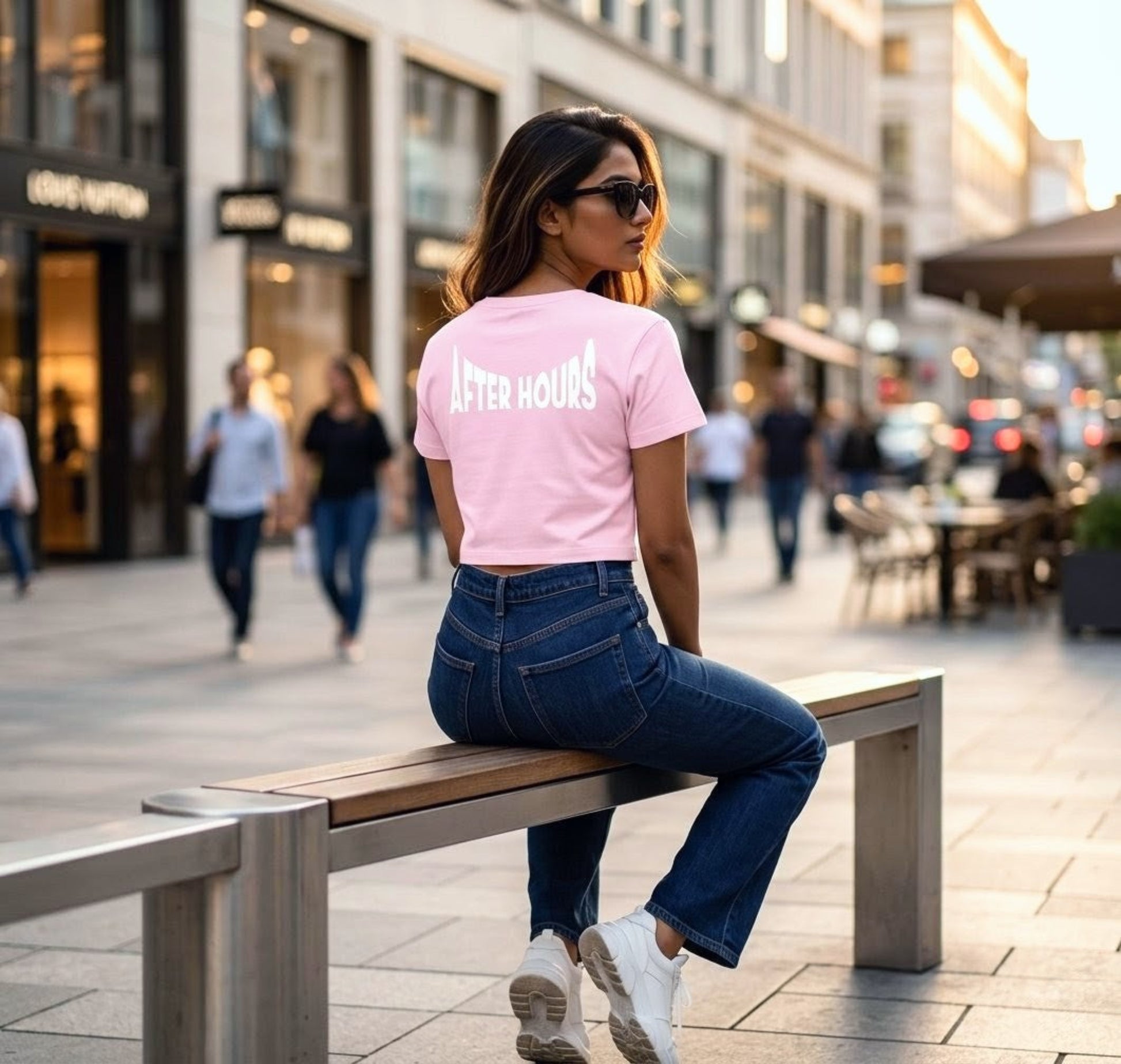 Woman sitting on a bench in an urban setting wearing a pink 'After Hours' t-shirt.