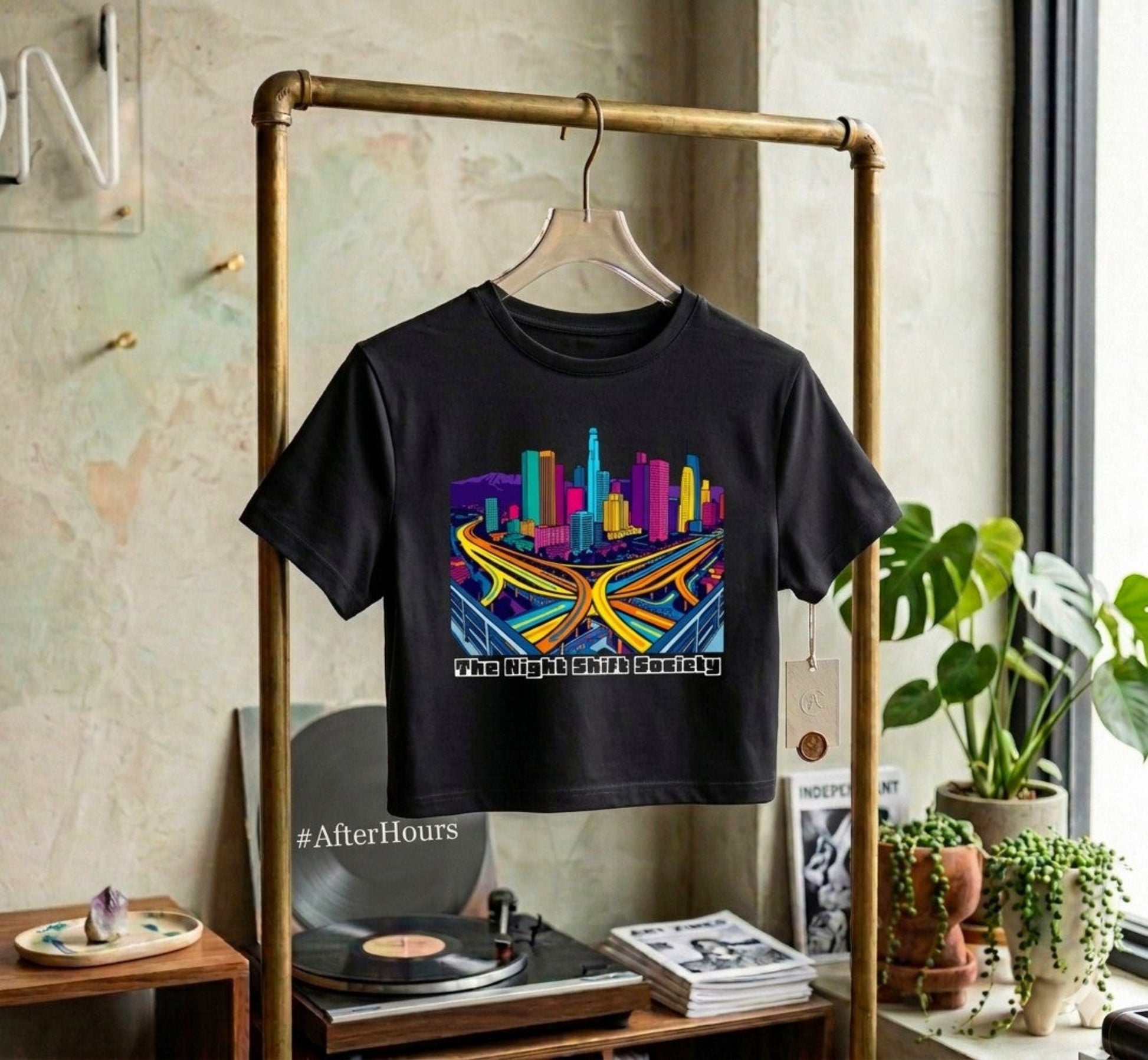 Black t-shirt with colorful graphic design hanging on a rack in a room with plants and records.