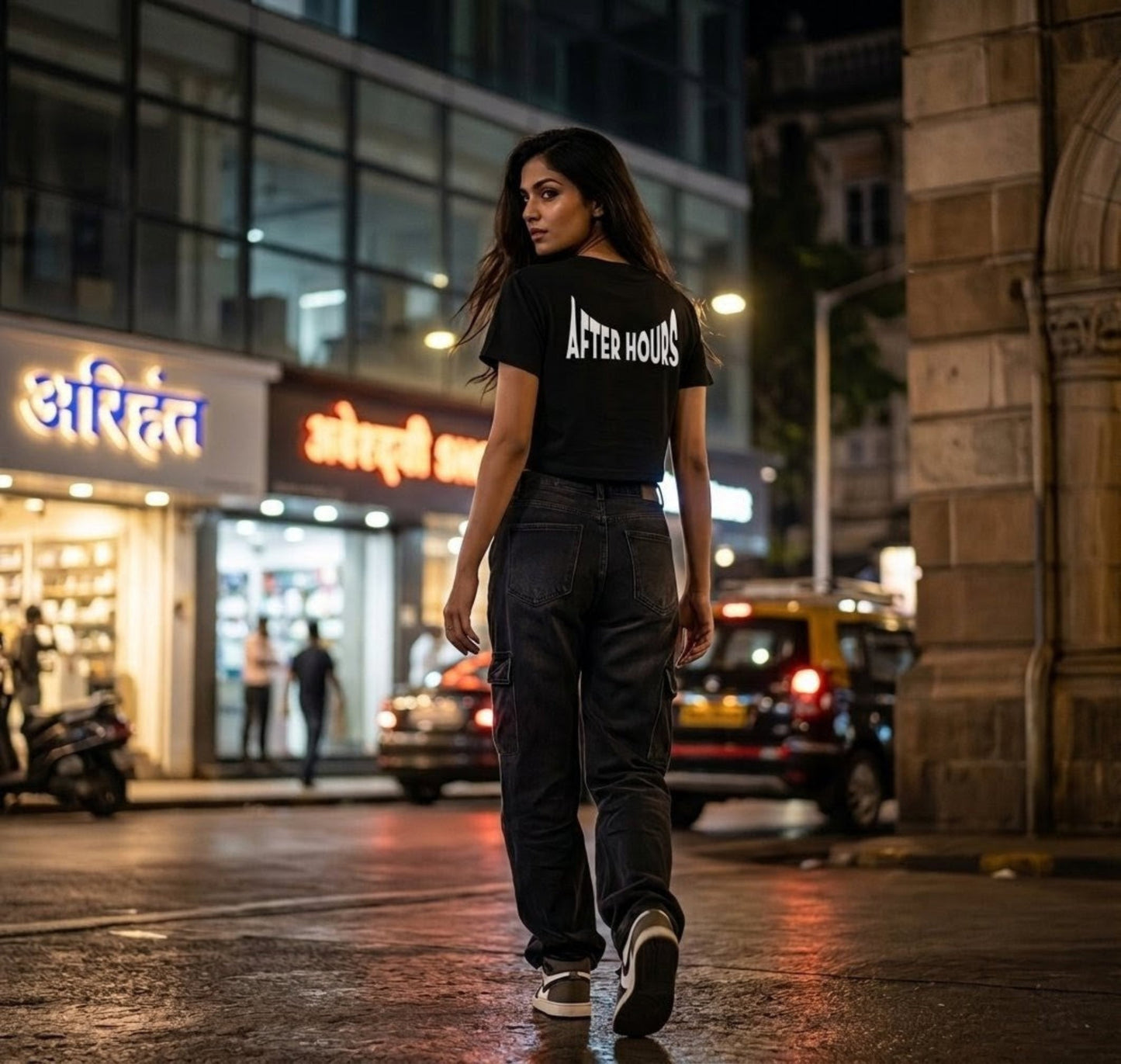 Woman walking on a city street at night wearing a black t-shirt with 'AFTER HOURS' text.