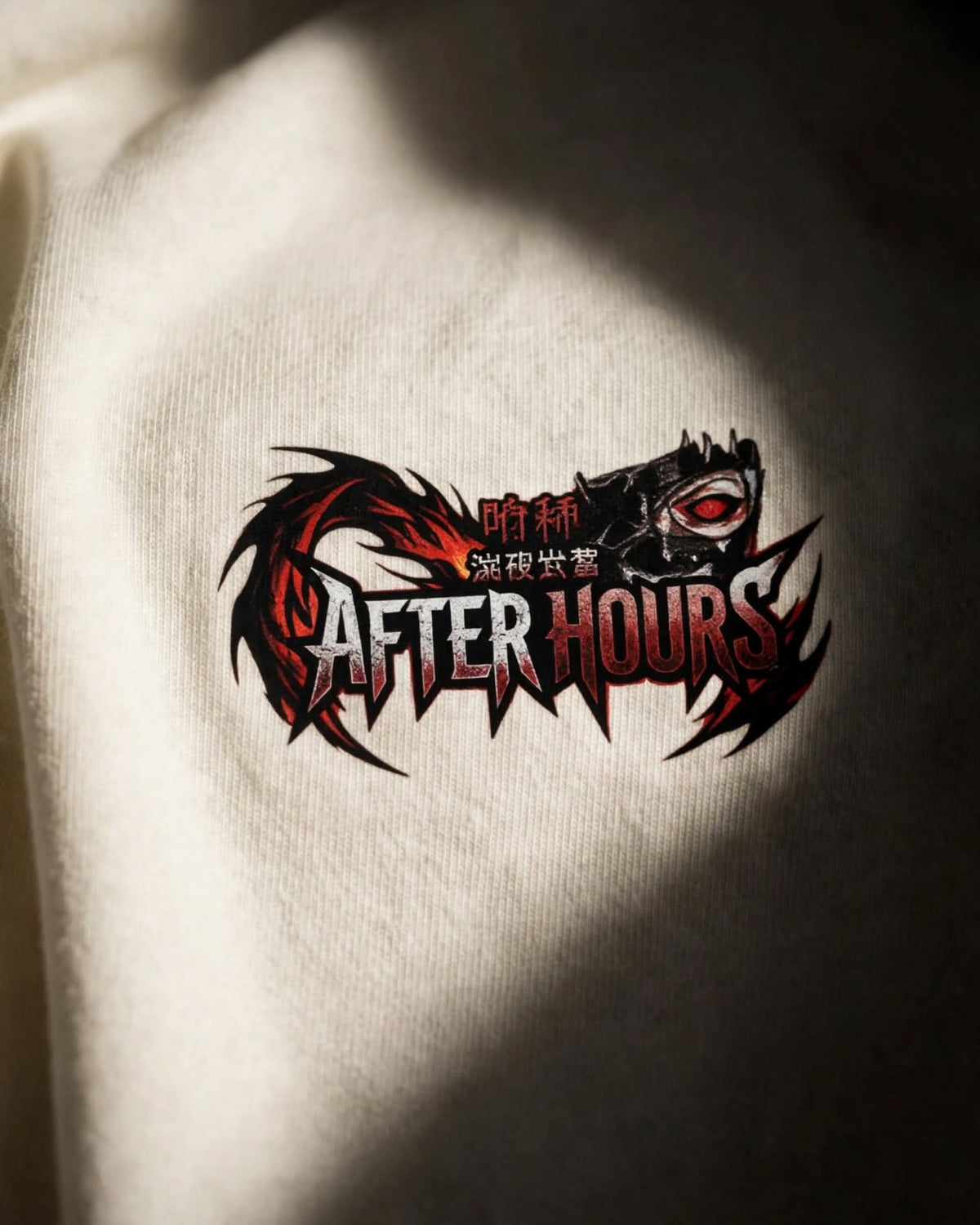 A close-up of a white tee, featuring a graphic print of the After Hours logo and red and black flame-like accents