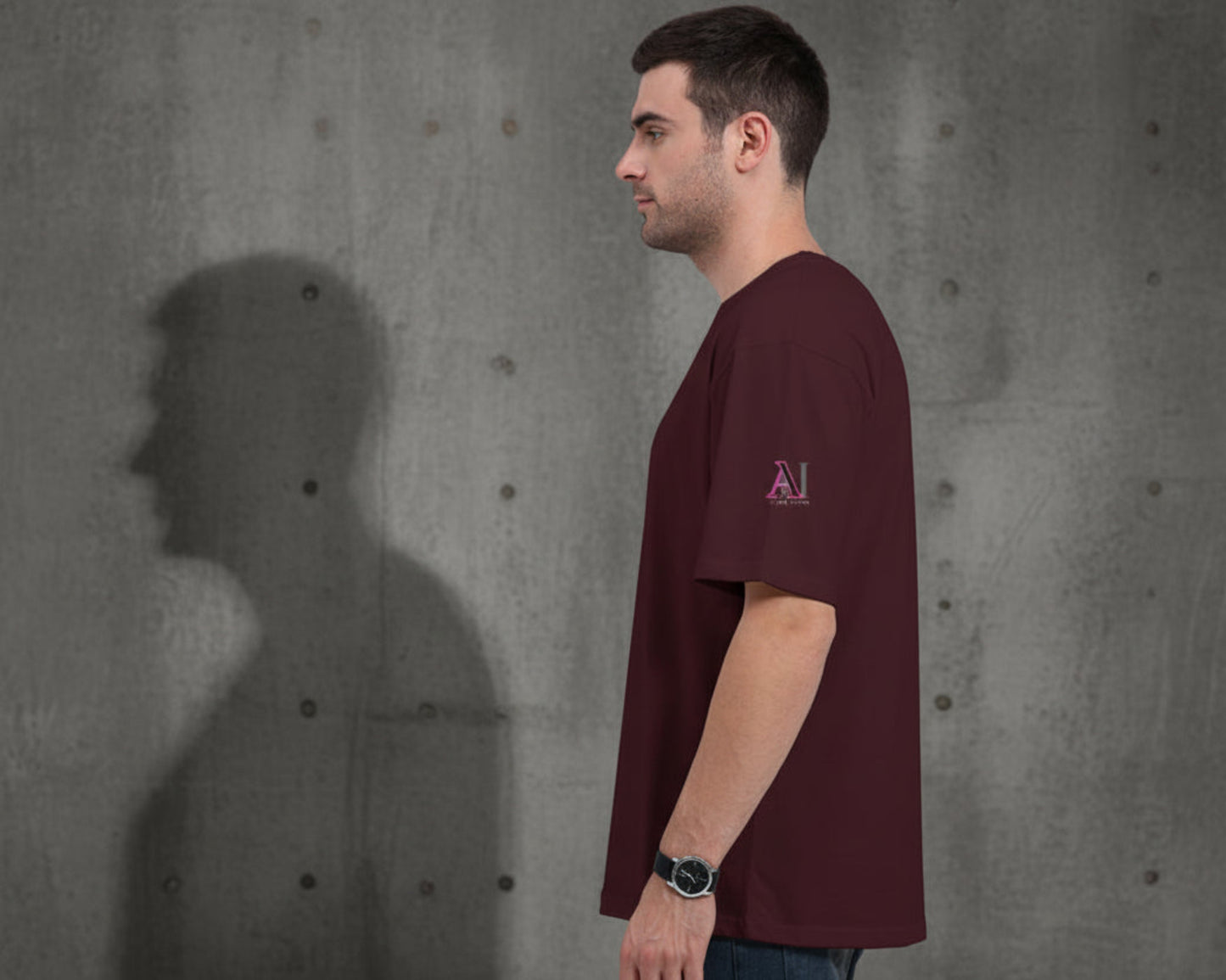 Man wearing a maroon t-shirt with a pink logo on a grey textured wall  background