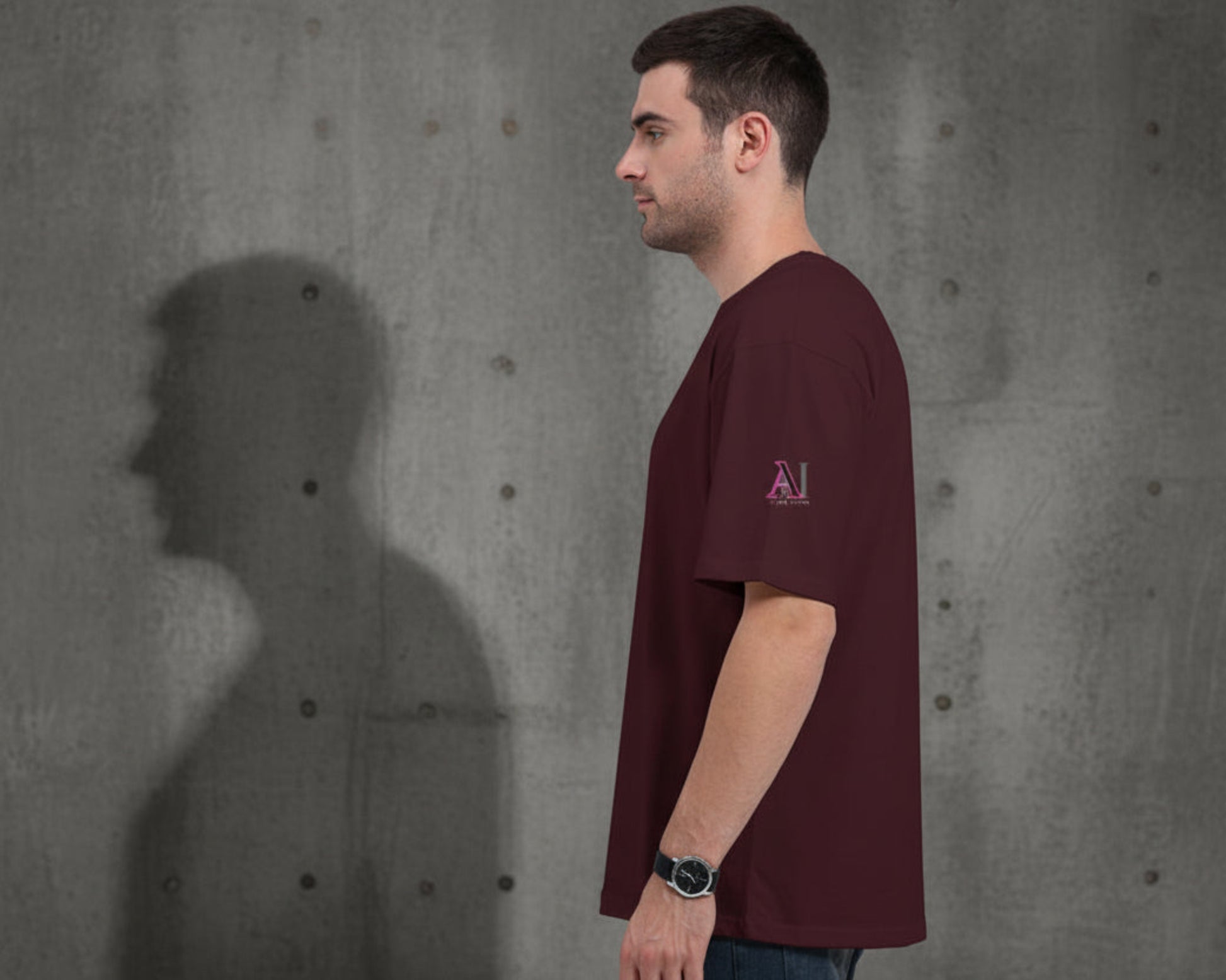 Man wearing a maroon t-shirt with a pink logo on a grey textured wall  background