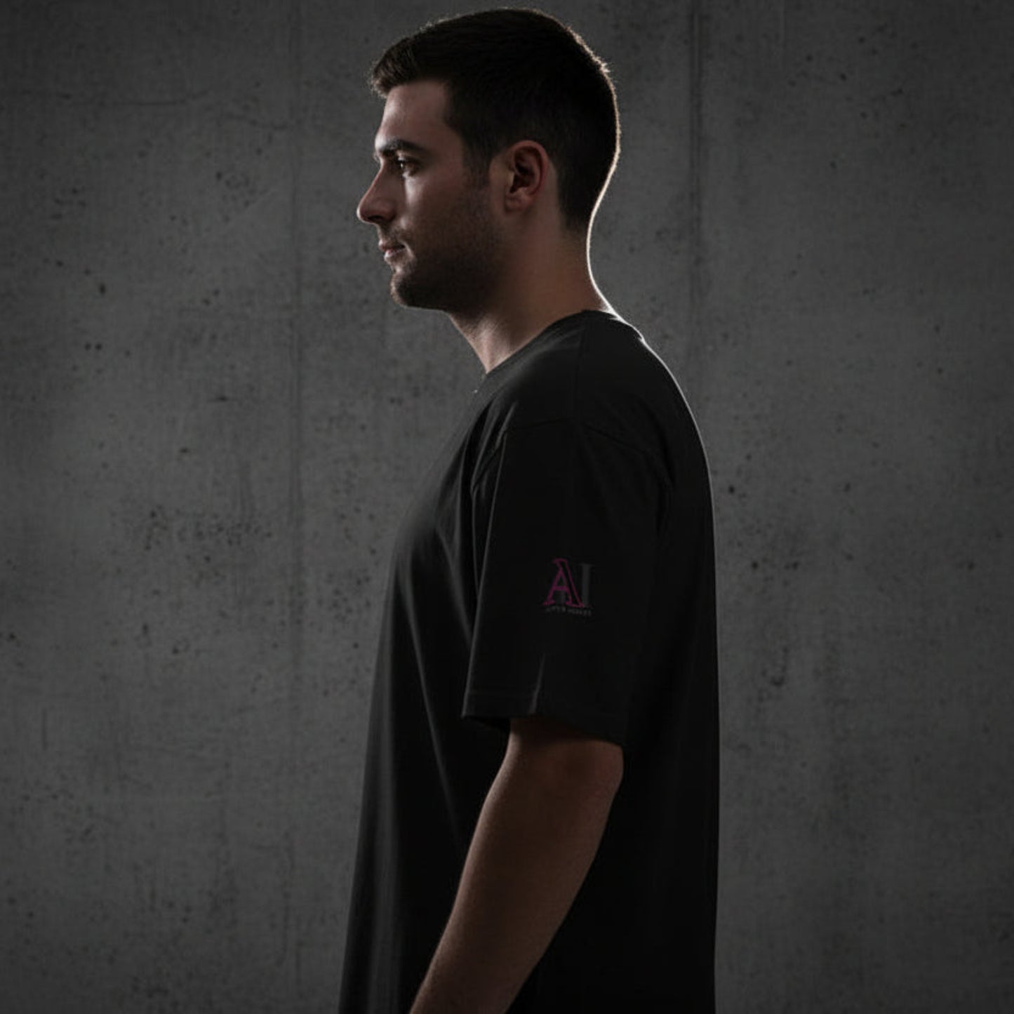 Man wearing a black t-shirt with a pink logo on a grey textured wall background