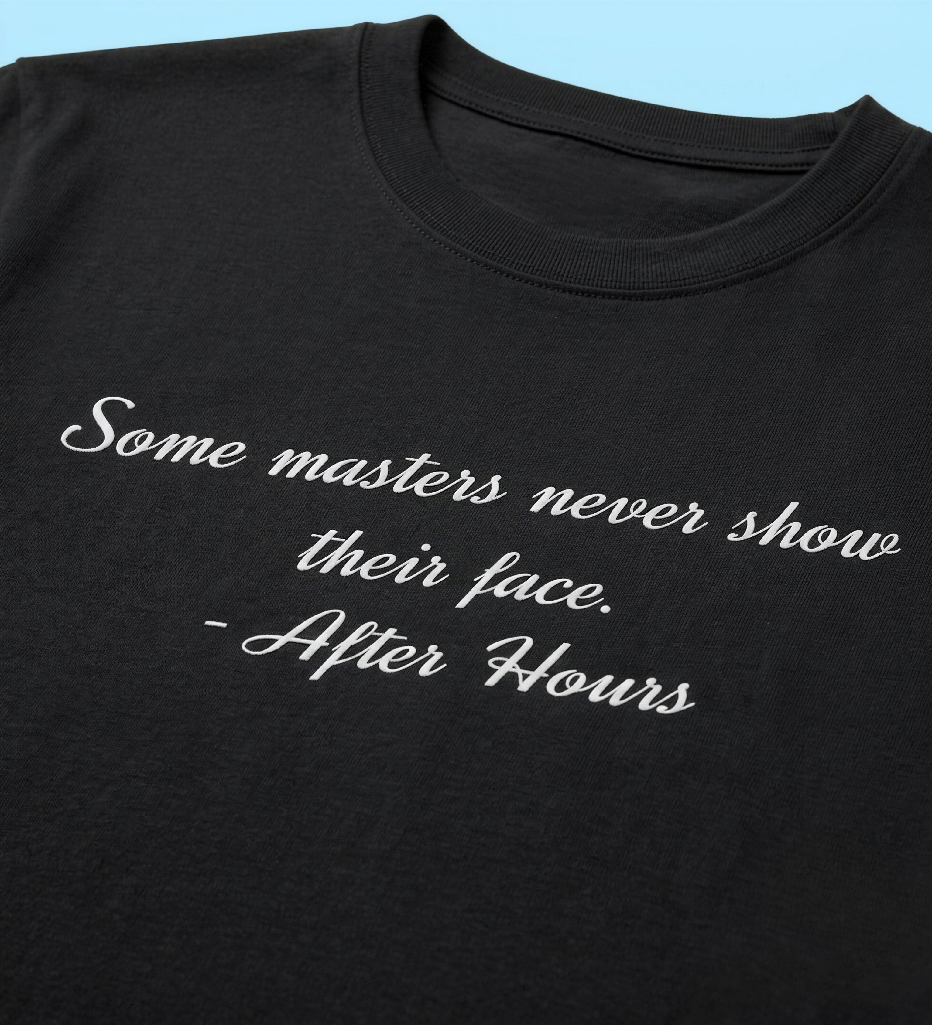A close-up of a black crewneck t-shirt featuring the quote 'Some masters never show their face. - After Hours' printed in white cursive text, set against a light blue background.