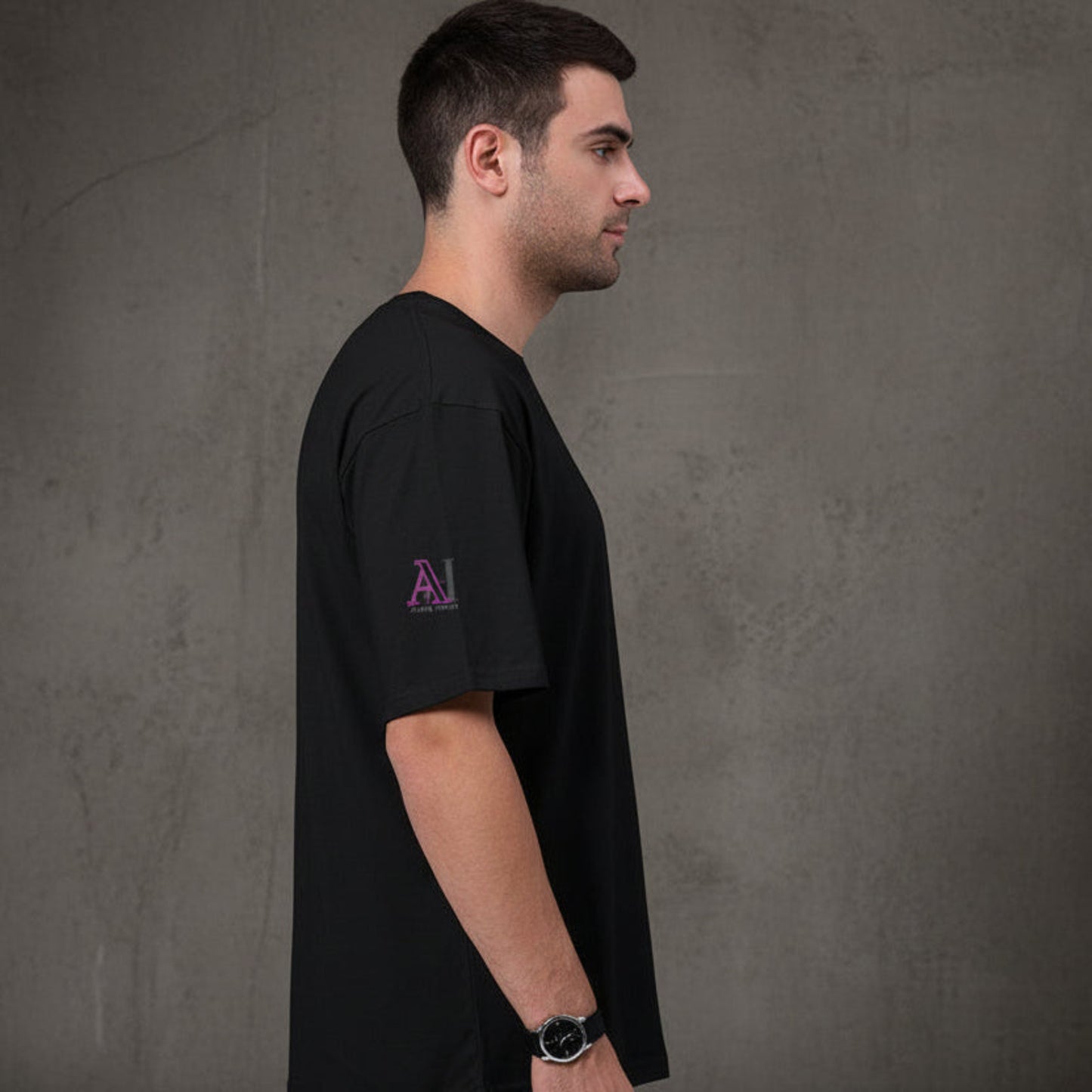 Man wearing a black t-shirt with a logo on the side against a grey textured wall background