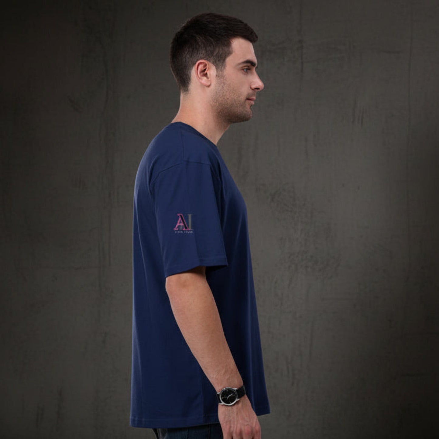 Man wearing a royal blue t-shirt with a logo on a grey textured wall background