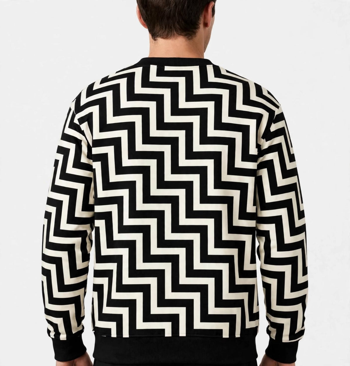 A man viewed from the back wearing a black and off-white zigzag patterned crewneck sweatshirt, set against a plain light grey background.