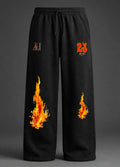 Black wide-leg sweatpants with a drawstring waist, featuring a stylized 'AH' logo on the right thigh, a red '23' on the left thigh, and realistic orange and yellow flame graphics on both legs, shown against a dark grey studio background.