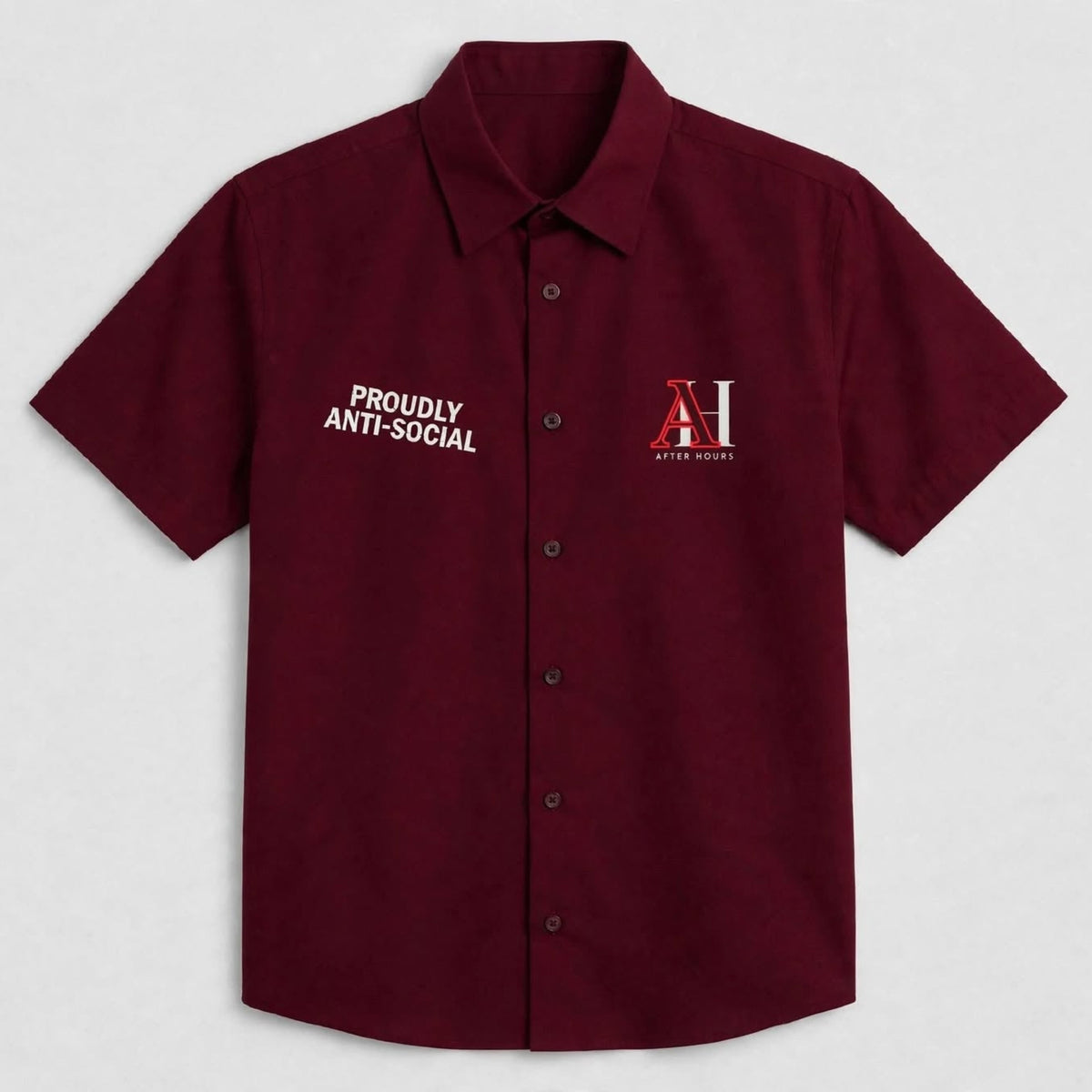 A short-sleeve button-up shirt in deep burgundy, featuring white text on the right chest reading 'PROUDLY ANTI-SOCIAL' and a red and white 'AH' logo on the left chest, displayed against a light grey background.