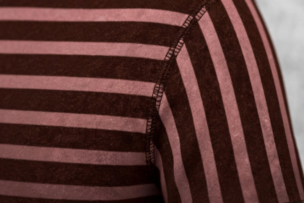 Close-up of a striped knit garment showing alternating dark brown and dusty pink horizontal stripes with a visible shoulder seam.