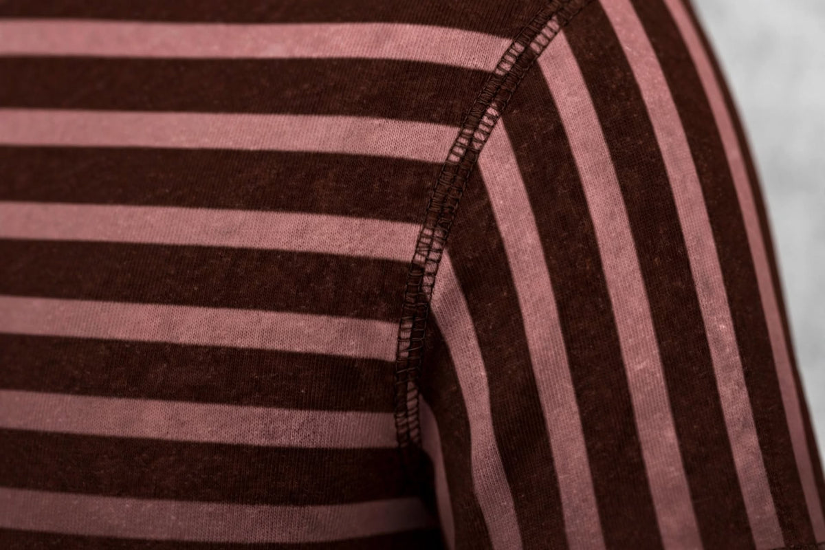 Close-up of a striped knit garment showing alternating dark brown and dusty pink horizontal stripes with a visible shoulder seam.