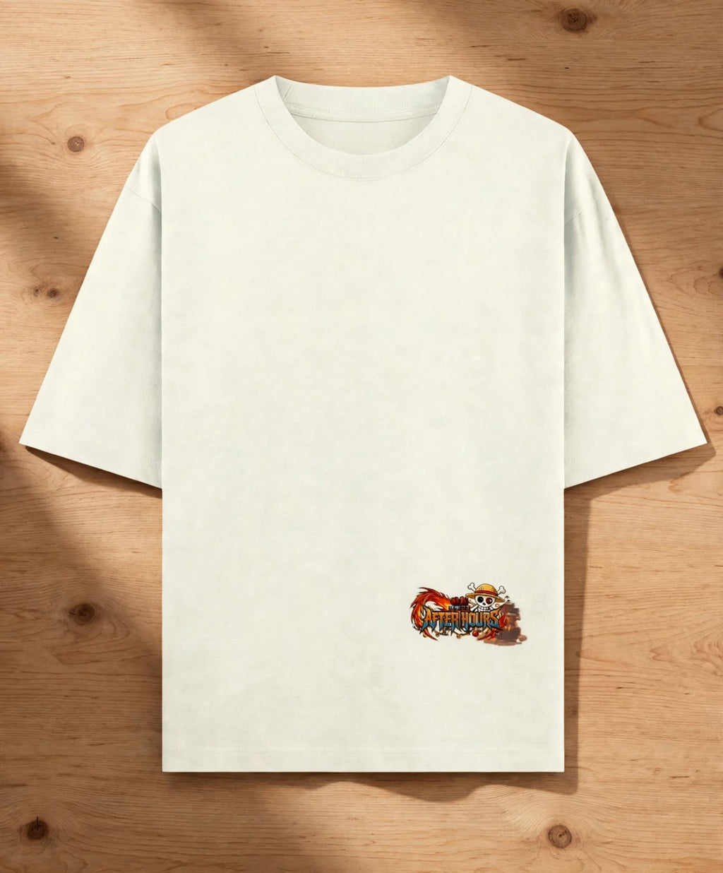 An off-white short-sleeve t-shirt with a small colorful graphic on the lower right front, displayed flat on a light brown wooden background.