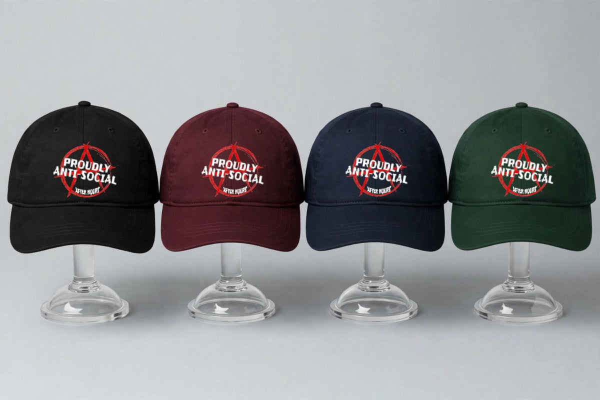 Four baseball caps displayed on clear stand bases against a light grey background. The caps are black, maroon, navy blue, and forest green, each featuring a white 'PROUDLY ANTI-SOCIAL' text with a red anarchy symbol.