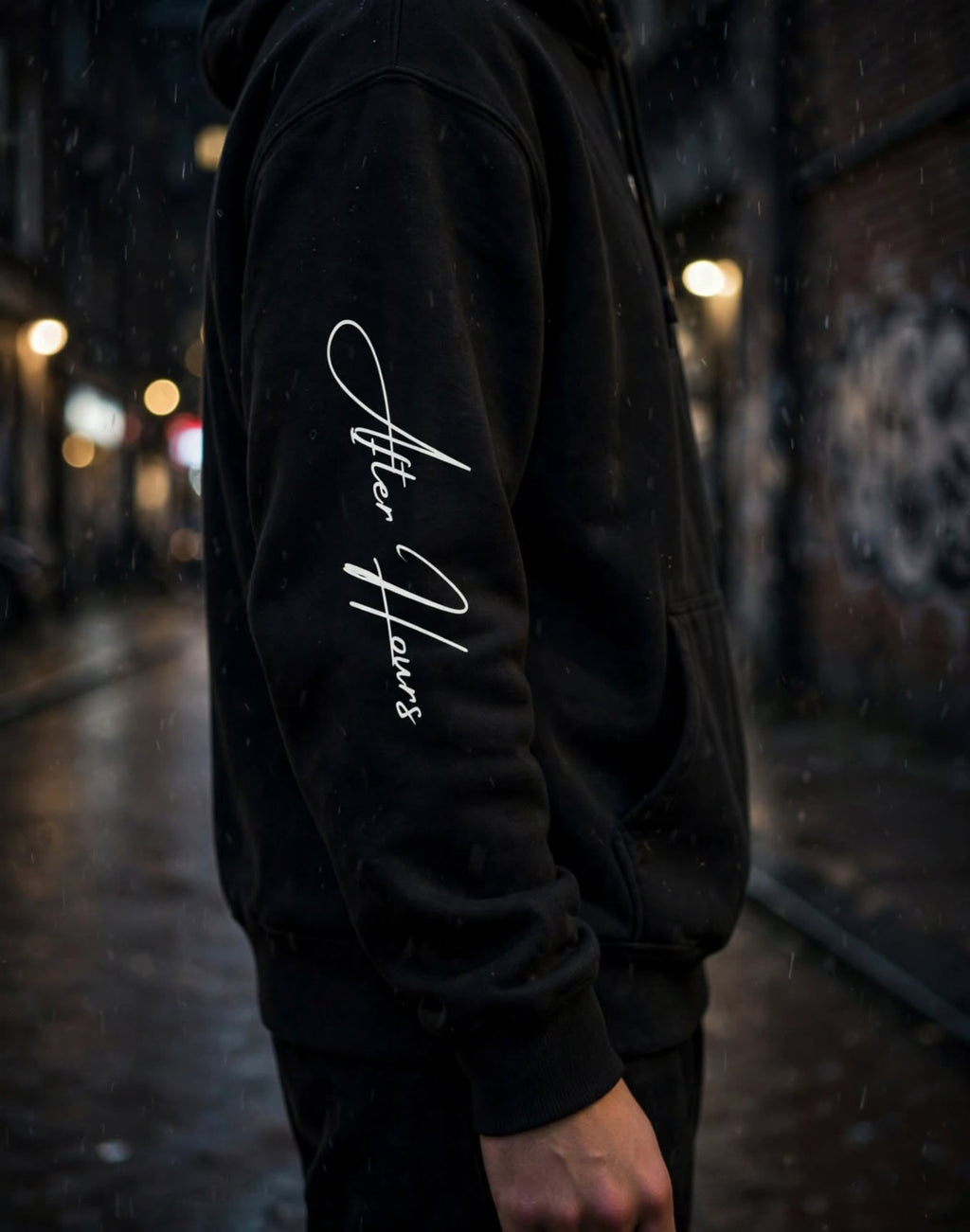 A person wearing a black hoodie in the rain on a city street, with white script text printed vertically on the left sleeve.