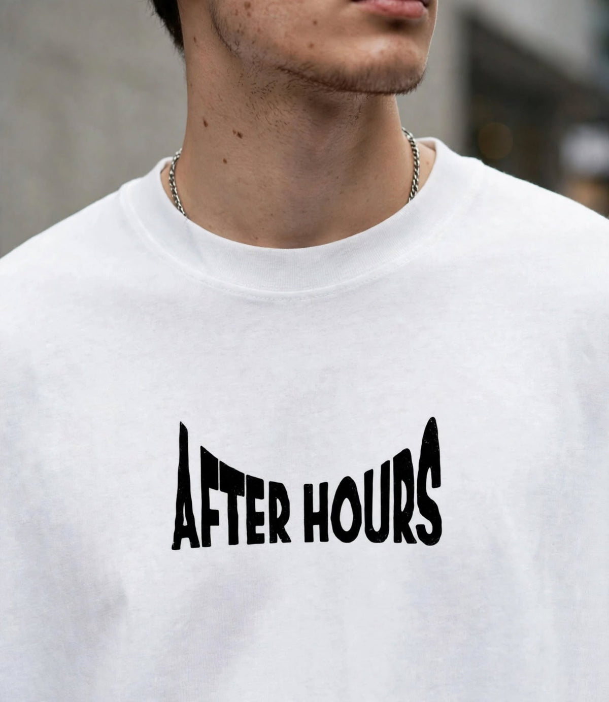 A close-up of a person wearing a white crewneck t-shirt with the words 'AFTER HOURS' printed in a stylized black font across the chest.