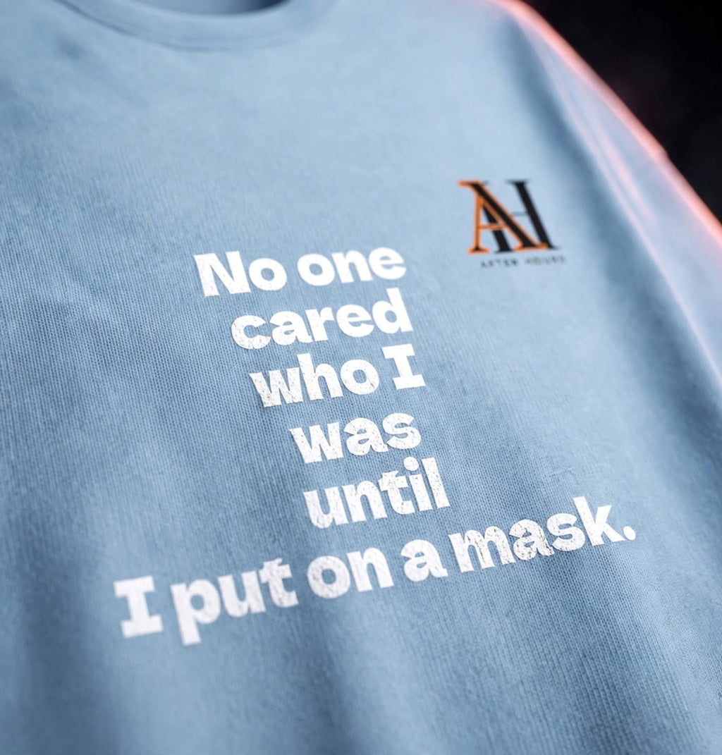 A close-up of a light blue t-shirt with white text that reads 'No one cared who I was until I put on a mask.' and a small 'AH AFTER HOURS' logo on the chest.
