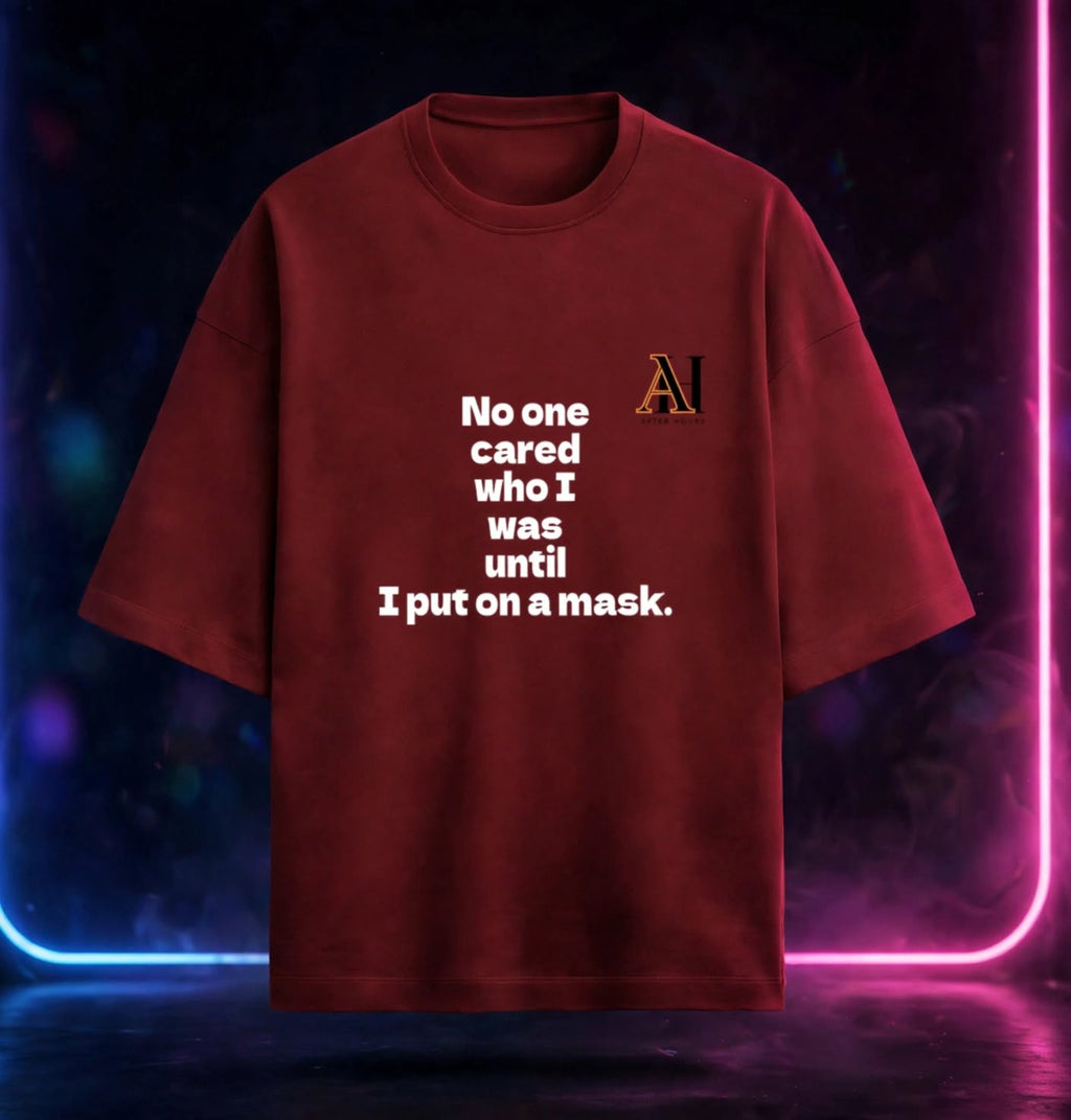 A dark red t-shirt with white printed text reading 'No one cared who I was until I put on a mask.' and a small 'AH' graphic in orange and black on the left chest, displayed against a dark background with neon blue and pink lights.