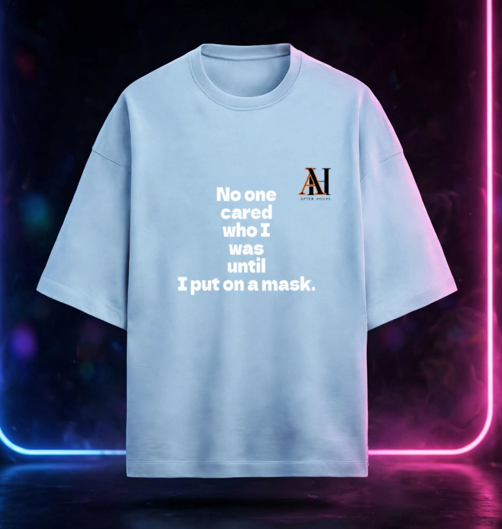 A light blue oversized t-shirt with white text reading 'No one cared who I was until I put on a mask.' and a small 'AH' logo on the left chest, displayed against a dark background with neon pink and blue light borders.