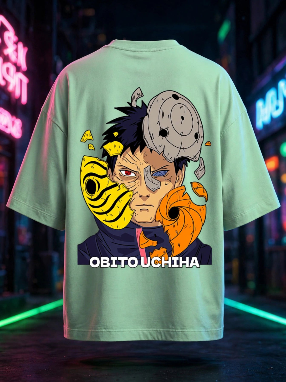A mint green short-sleeve t-shirt featuring a large graphic print of the anime character Obito Uchiha on the back, with his Sharingan and Rinnegan eyes and the text 'OBITO UCHIHA' printed below. The shirt is displayed against a dark, neon-lit city street background.
