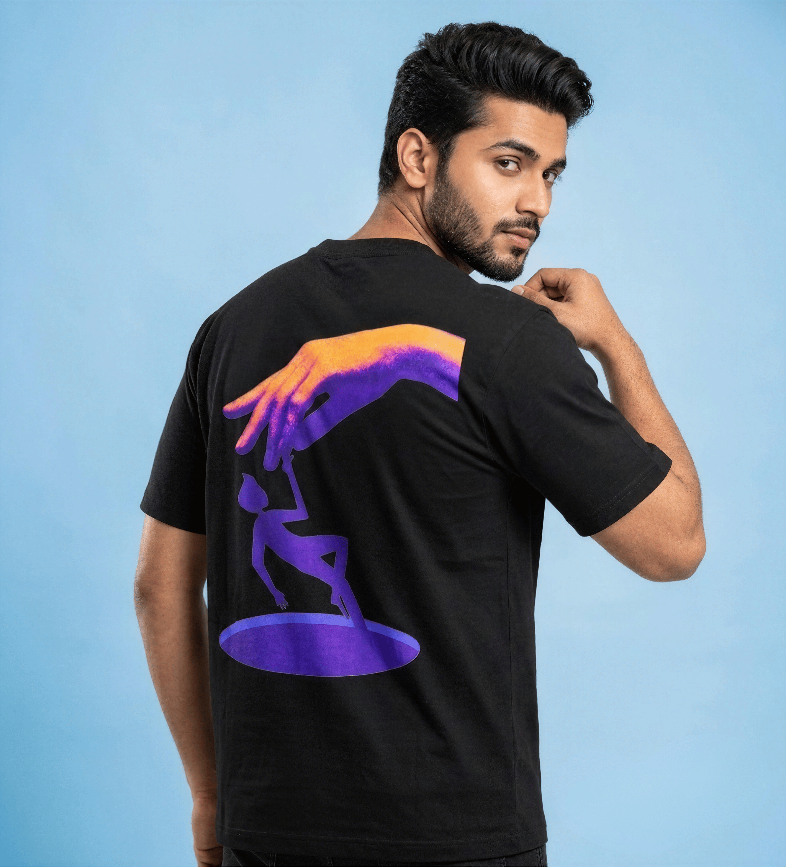 A man wearing a black t-shirt with a colorful graphic print on the back, posing against a solid light blue background.