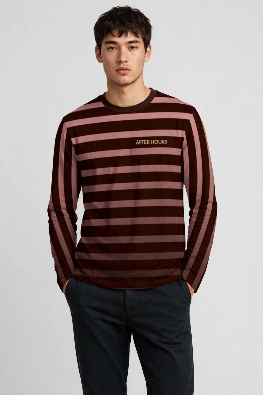 A man wearing a long-sleeve striped knit top with dark brown and dusty rose horizontal stripes, featuring the 'AFTER HOURS' logo on the chest, paired with dark trousers, against a light grey studio background.
