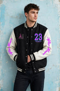A man wearing a black and cream varsity jacket with pink and blue lettering, posing against a textured light blue wall.