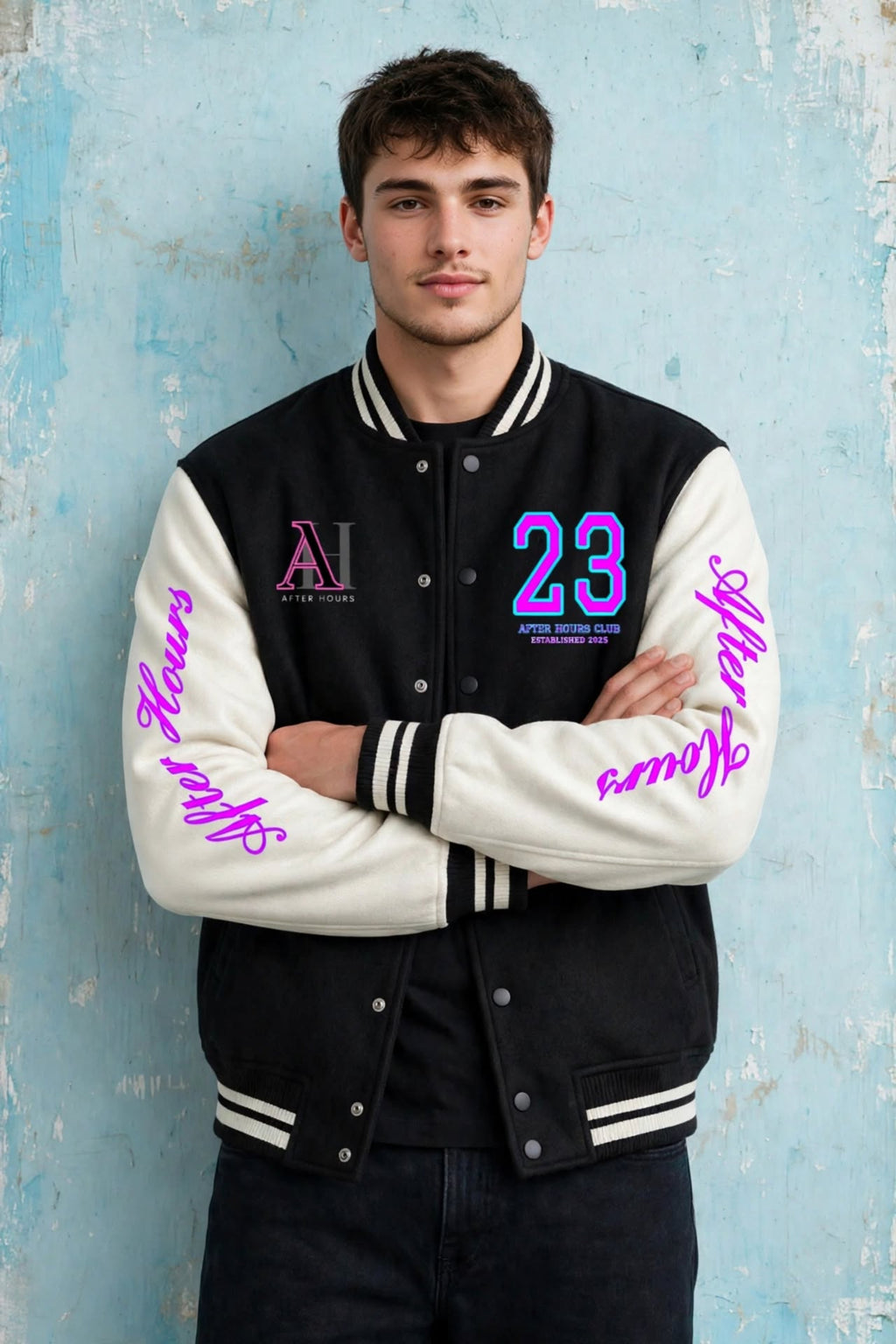 A young man stands with arms crossed wearing a varsity-style jacket with black body panels and white sleeves, featuring pink lettering and the number 23 on the chest, posed against a textured light blue wall.